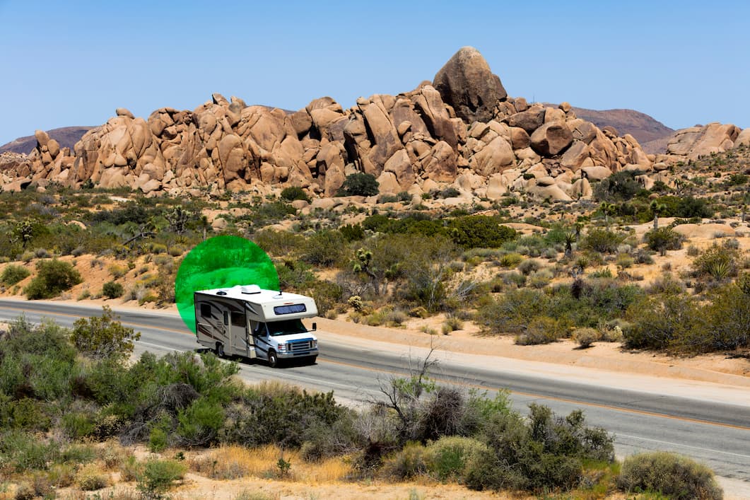 White and gray Class A motorhome driving on desert highway surrounded by scrub brush and arid terrain