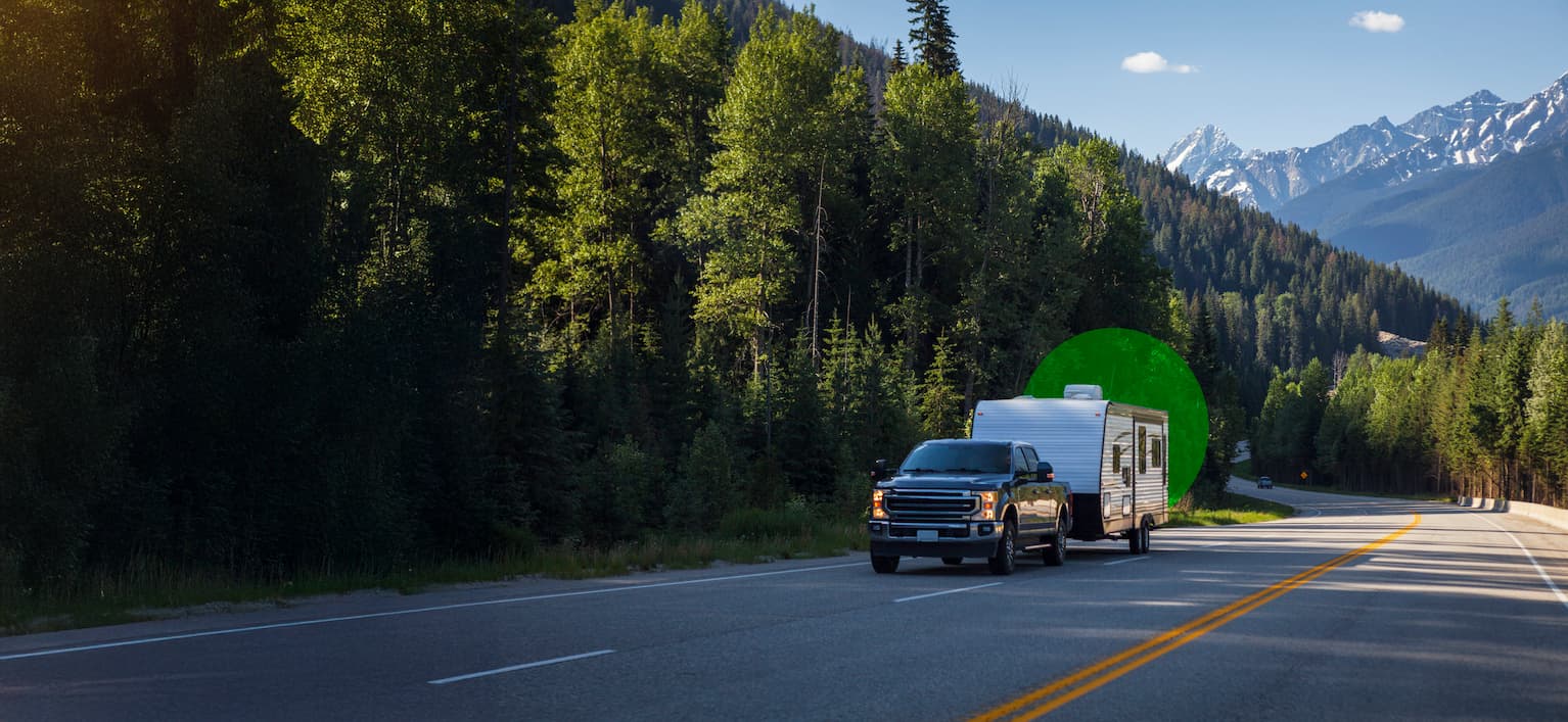 Pickup truck towing travel trailer on paved highway with yellow center lines through forested area